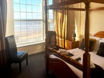 a bedroom with a bed and a chair and a window at The President Hotel in Blackpool
