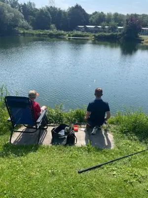 two men sitting on a bench next to a lake at Lakeland Lodge 9B Arnside , Carnforth ,Lancaster , LA61BH in Carnforth