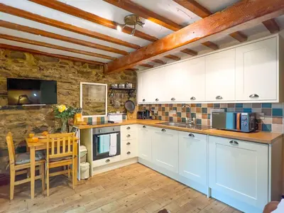 a kitchen with white cabinets and a table and chairs at The Stable, Broughton Beck, a ground floor cottage close to a beach and Windermere in Spark Bridge