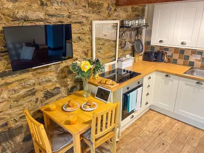 a kitchen with a wooden table and a television at The Stable, Broughton Beck, a ground floor cottage close to a beach and Windermere in Spark Bridge