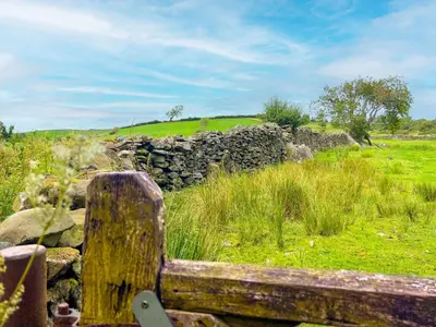 a wooden bench in a field with a stone wall at The Stable, Broughton Beck, a ground floor cottage close to a beach and Windermere in Spark Bridge