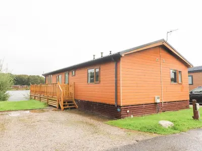a large wooden house with a porch in a yard at Lakeside 12 in Carnforth