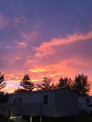 a sunset over a white trailer with trees in the background at Haven Lakeland 3 Bed Luxury Caravan in Flookburgh