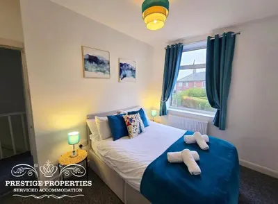 a bedroom with a bed with blue sheets and a window at 8 Suffolk street by Prestige Properties SA in Barrow in Furness