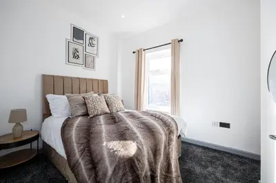 a bedroom with a bed with a blanket and a window at Deluxe Bolton Cinema House 2BR Modern Retreat with Free Parking in Bolton