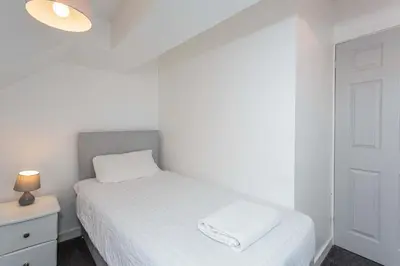 a white bedroom with a bed and a nightstand with a lamp at Cherry Property - Blueberry Suite in Blackpool