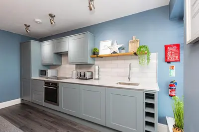 a kitchen with gray cabinets and blue walls at Seafront Apartment - Sleeps 6 - Gateway to the Lake District - Brand New in Morecambe