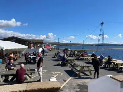 a group of people sitting at picnic tables by the water at Apartment 1 West County by Prestige Properties SA in Millom