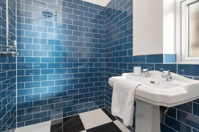 a blue tiled bathroom with a sink and a mirror at Ettie and Gigi's in Blackpool