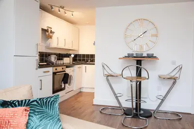 a kitchen and a living room with a clock on the wall at Penthouse - Liverpool City Centre - NHS STAYS - Liverpool Royal Hospital in Liverpool