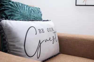 a pillow that says be our guest sitting on a couch at Penthouse - Liverpool City Centre - NHS STAYS - Liverpool Royal Hospital in Liverpool