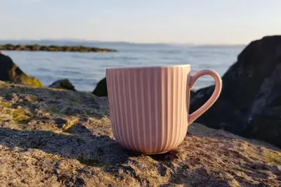 a white coffee cup sitting on a rock near the ocean at 4 Bed house Sea Views Benji's by the beach in Morecambe