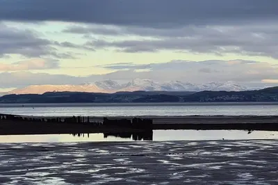 a body of water with snow capped mountains in the background at 4 Bed house Sea Views Benji's by the beach in Morecambe