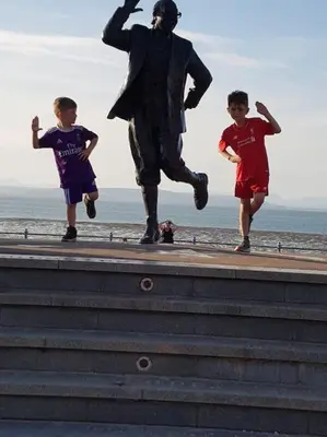 two boys running past a statue on the beach at 4 Bed house Sea Views Benji's by the beach in Morecambe