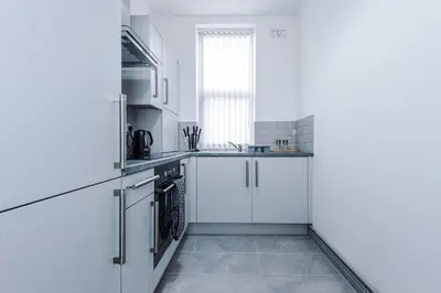 a white kitchen with white cabinets and a window at 5 Sleeper LFC Themed Apartment in Liverpool