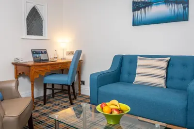 a living room with a blue couch and a table with a bowl of fruit at Last Drop Village Hotel & Spa in Bolton