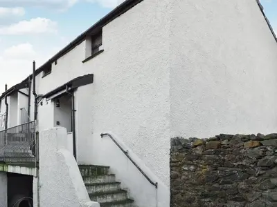 a white building with stairs leading up to a door at Beck Cottage in Millom