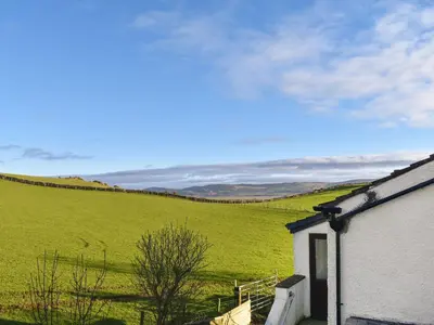 a house in a green field with a hill behind it at Beck Cottage in Millom