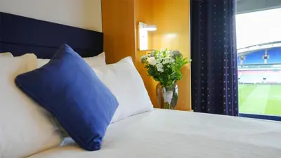a bed with a blue pillow and a vase of flowers at The Bolton Stadium Hotel, a member of Radisson Individuals in Bolton