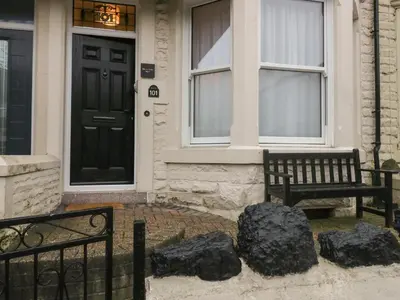 a house with a black door and two benches at West End Bay in Morecambe