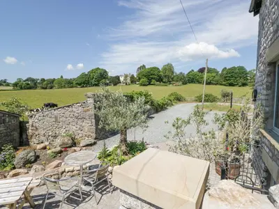 a patio with a table and chairs and a stone wall at Old Watermill in Grange Over Sands