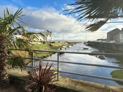 a river next to a fence with houses and condos at 23 Coastal Comfort in Millom