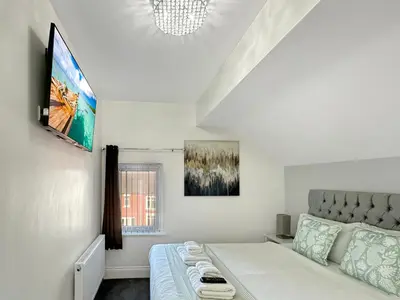 a white bedroom with a bed and a flat screen tv at Granada Apartments Holmfield Rd in Blackpool