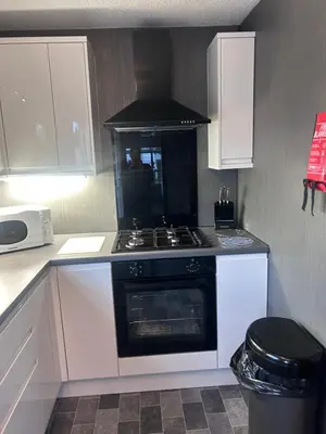 a kitchen with a stove and white cabinets at Sunshine Lodge Haven Lakeland in Flookburgh