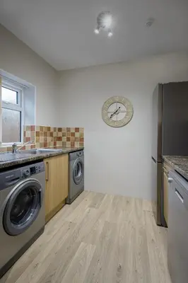 a kitchen with a washing machine and a clock on the wall at Arnside - Spacious 10-Bedroom Seaside Cottage in Blackpool