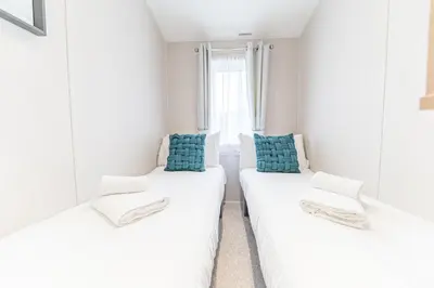 two beds in a white room with blue pillows at Tastefully decorated lodge on popular holiday park, easy access to Lakes and Dales and free parking in Carnforth