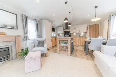 a living room with a fireplace and a kitchen at Tastefully decorated lodge on popular holiday park, easy access to Lakes and Dales and free parking in Carnforth