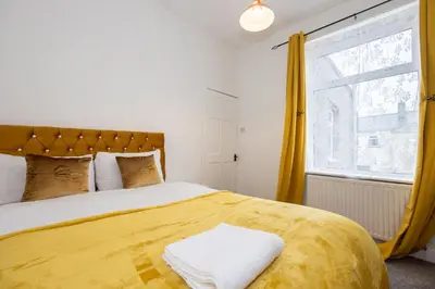 a bedroom with a large bed with yellow curtains at Cosy Four Bedroom Terrace Rishton in Rishton