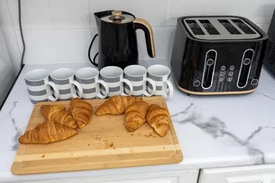 a cutting board with croissants and cups on a counter at Cosy Four Bedroom Terrace Rishton in Rishton