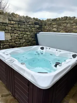 a large bath tub sitting next to a stone wall at Converted Barn with Hot Tub, The Hayloft. in Carnforth