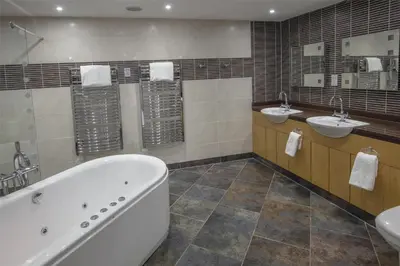 a bathroom with two sinks and a tub and two mirrors at Best Western Premier Suites Hotel & Spa Liverpool-Knowsley in Knowsley