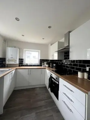 a kitchen with white cabinets and a wooden floor at No. 10 - Home away from Home in Litherland