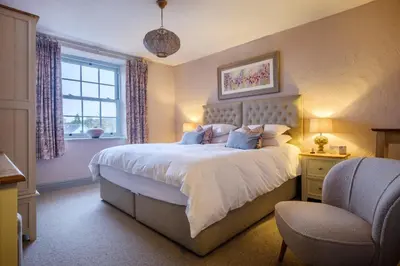 a bedroom with a bed and a chair and a window at Sunny Brae in Grange Over Sands