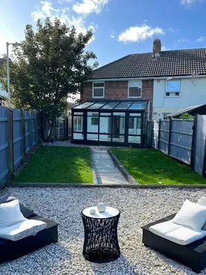 a backyard with two chairs and a house with a fence at Bright 3 bedroom house with conservatory in Birkenhead