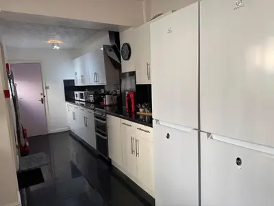 a white kitchen with white cabinets and black appliances at Winter Gardens large modern home in Blackpool