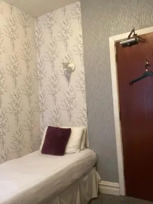 a small bedroom with a bed and a wall with wallpaper at Iona Hotel in Blackpool