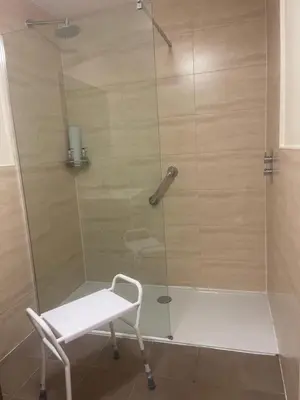 a shower with a glass door with a white stool at The Chetwynde - Self Check In HMO in Barrow in Furness