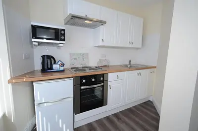 a small kitchen with white cabinets and a black appliance at Twelve Apartments in Blackpool