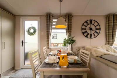 a dining room with a table and chairs with a clock at Wiswell View Lodge: Pendle View Holiday Park in Clitheroe