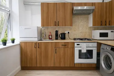 a kitchen with wooden cabinets and a washer and dryer at Sidemersey Livings - Botanic Residence in Liverpool