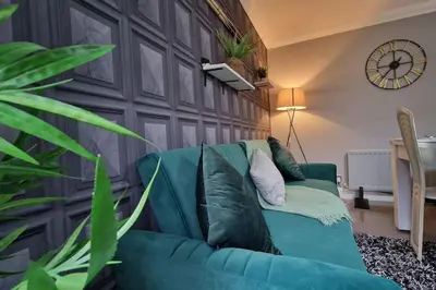 a green couch in a living room with a clock on the wall at Great Liverpool Location! in Liverpool