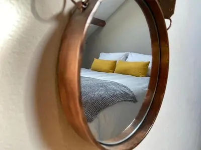 a mirror reflecting a bed with yellow pillows at Cartmel Barn: Beckside Stables in Cartmel