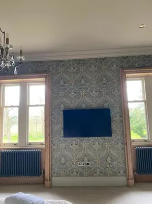 a room with a tv on a wall with two windows at Home Farm Cottage in Lytham St Annes
