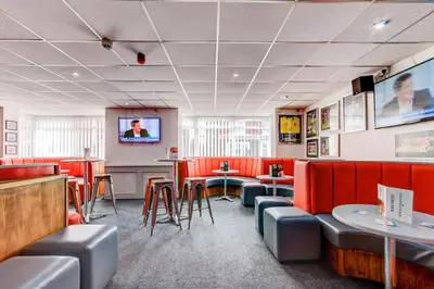 a restaurant with red booths and tables and a flat screen tv at The Sandringham Court Hotel & Apartment Welcoming Large and Small Groups for 16 years in Blackpool