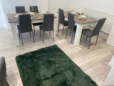 a dining room table with chairs and a green rug at Stylish Home - Close to City Centre, Anfield Stadium - Free Parking in Litherland