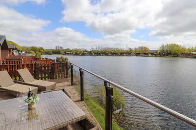 a patio with a table and chairs next to a body of water at Capenwray in Carnforth